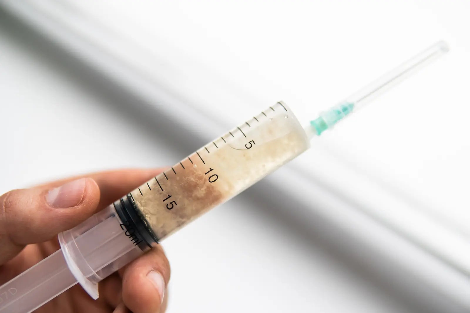Hand houdt een spuit gevuld met troebele vloeibare myceliumcultuur vast