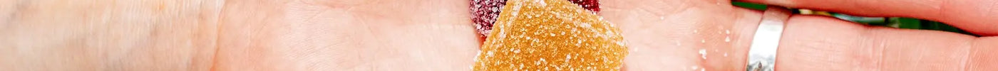 Twee THC gummies in een hand met cannabisplanten op de achtergrond
